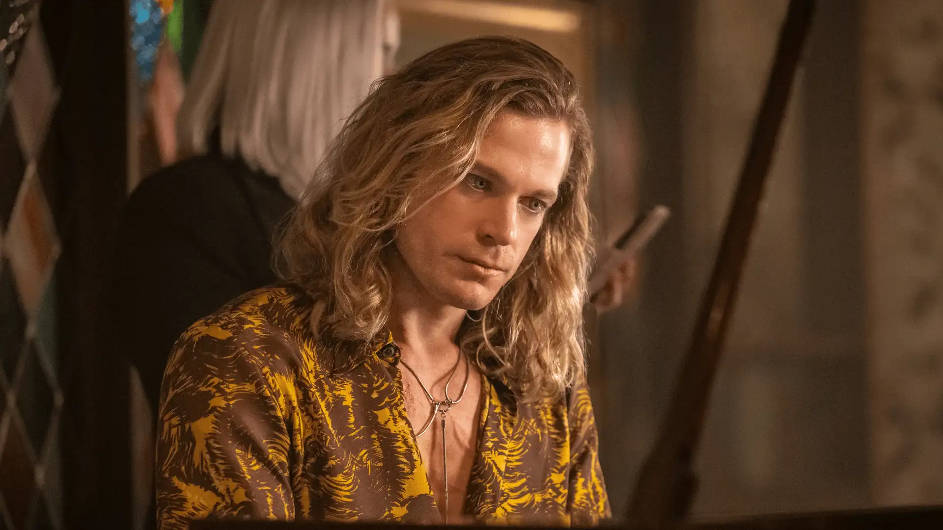 The Vampire Lestat Szene: Langhaarige Figur sitzt am Klavier in elegantem goldbraunen Hemd, warmes Licht, intime Atmosphäre im Innenraum