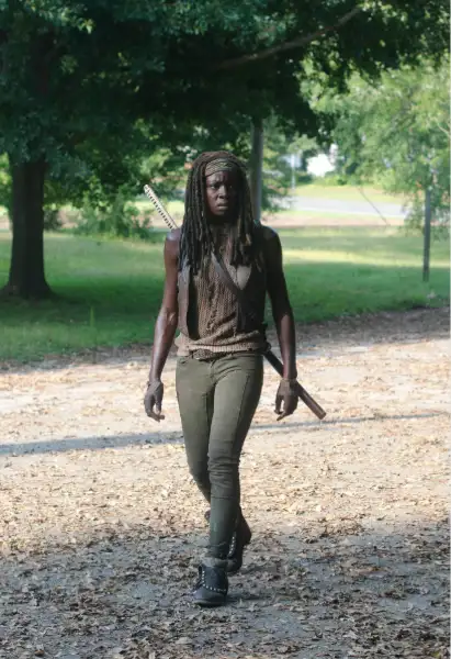 Danai Gurira als Michonne Jones in The Walking Dead. Sie trägt eine grüne Hose, eine braune lederjacke und ein dunkelbraunes Shirt darunter. Auf ihrem Rücken befindet sich ihr Katana.