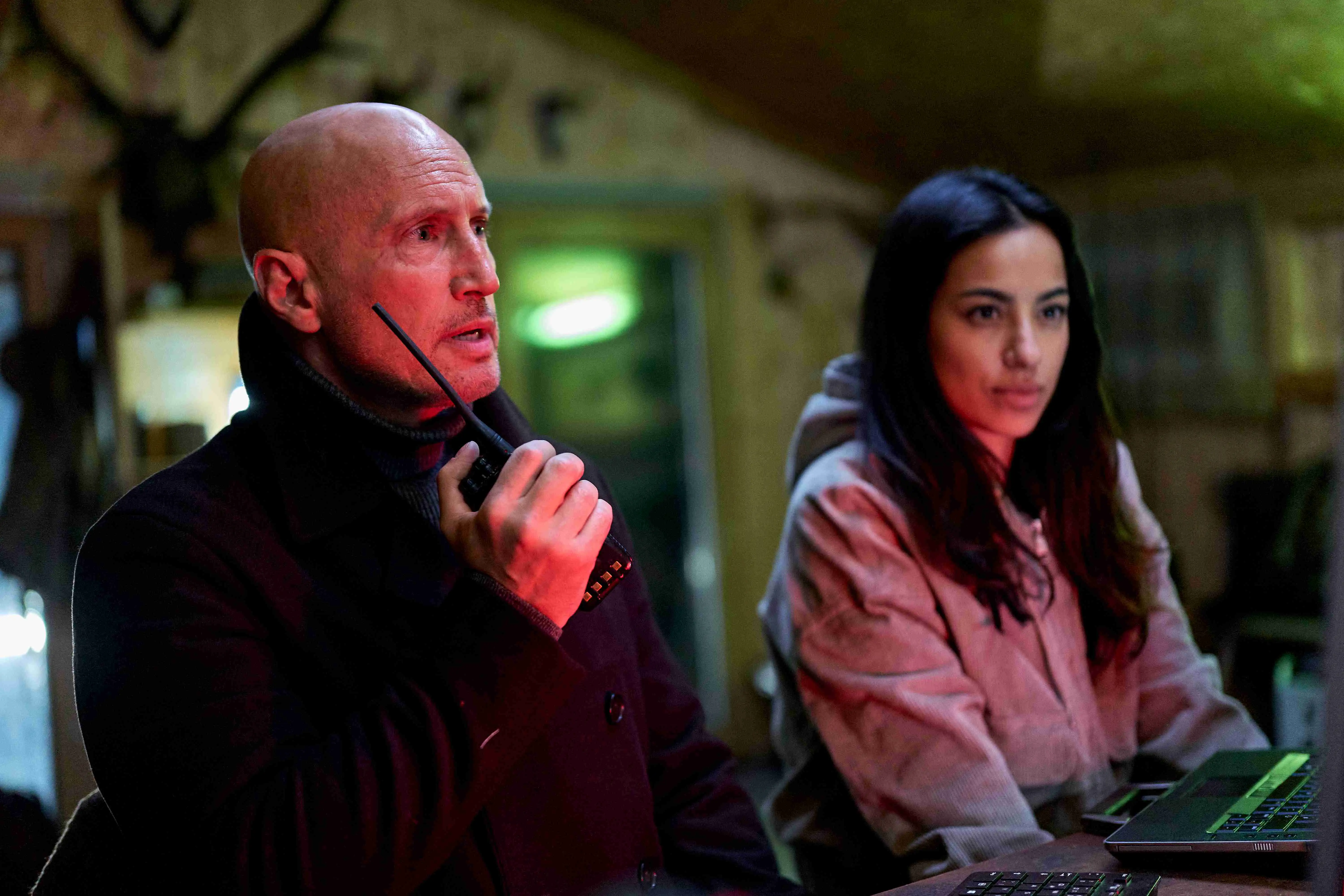 Benno Fürmann als Thilo Mannheim in Neo Nuggets, mit Funkgerät in einer nächtlichen Szene, neben Samira Leoni am Laptop unter rotem und grünem Licht.