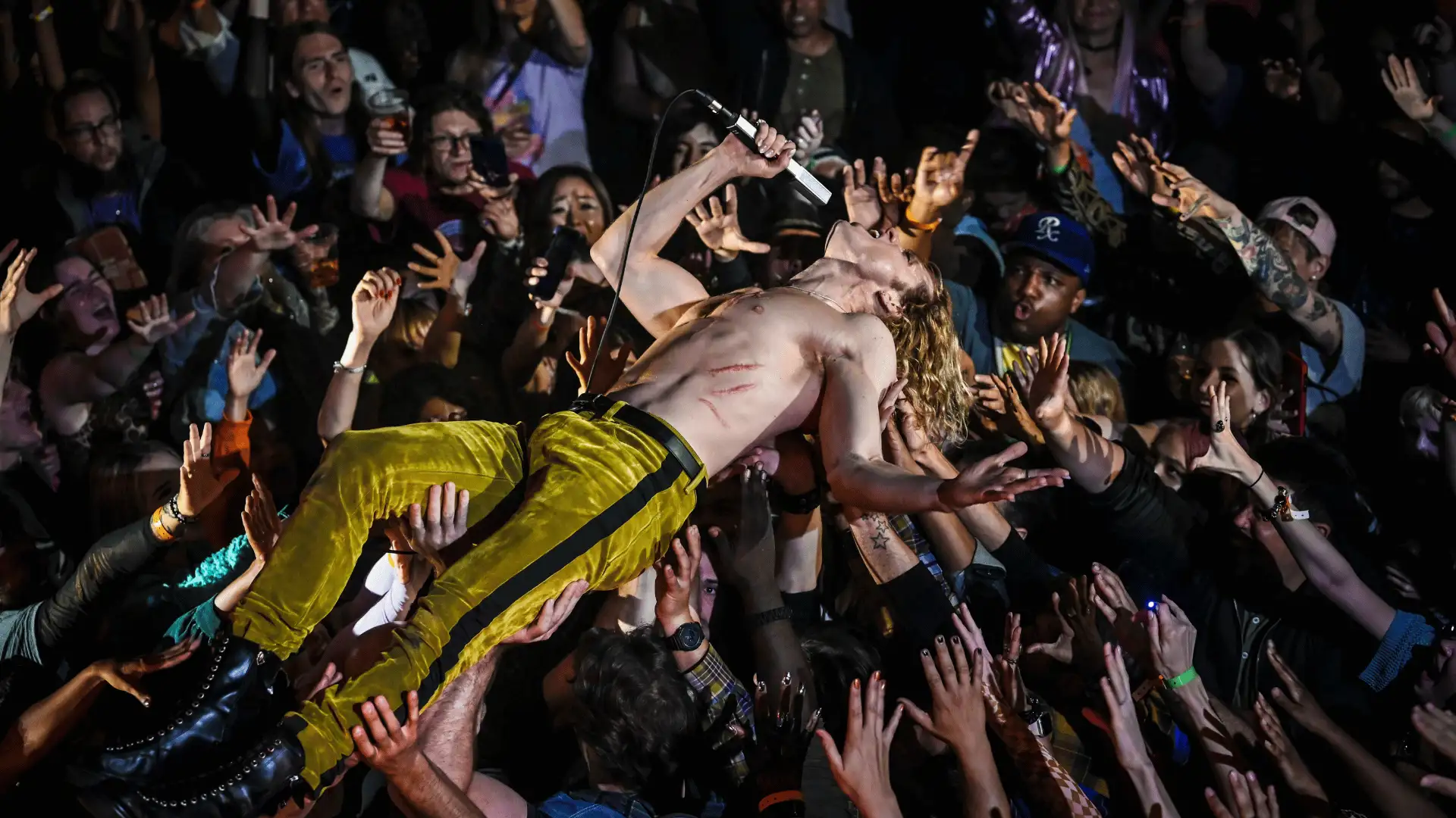 The Vampire Lestat Konzertszene: Rock-Sänger Oberkörperfrei beim Crowdsurfen in dunkler Konzertathmosphäre.