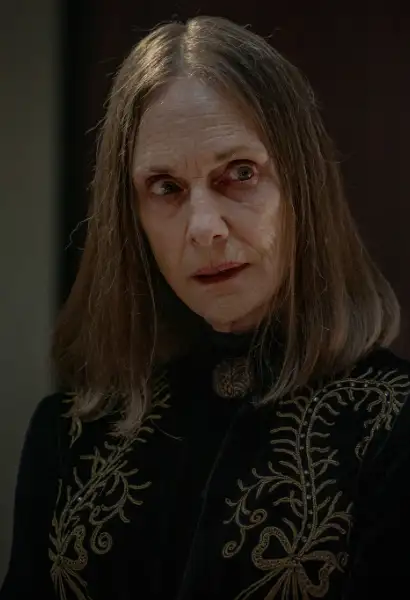 Lisa Emery als The Dama in Dead City. Sie trägt ein dunkles, verziertes Kleid. Sie hat einen besorgten Blick.