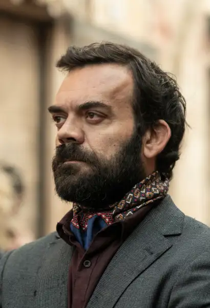 Gonzalo Bouza als Guillermo Torres in The Walking Dead: Daryl Dixon. Er trägt ein graues Sakko, ein dunkelrotes Hemd und ein buntes Halstuch.