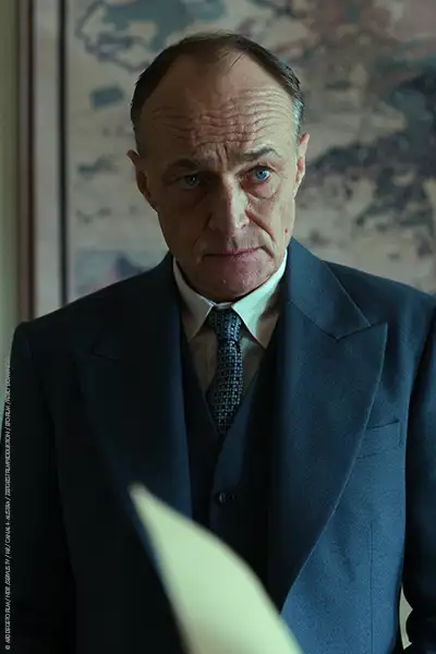 Karel Dobrý als Beran im blauen Anzug, der Hintergrund scheint eine Weltkarte in seinem Büro zu zeigen.