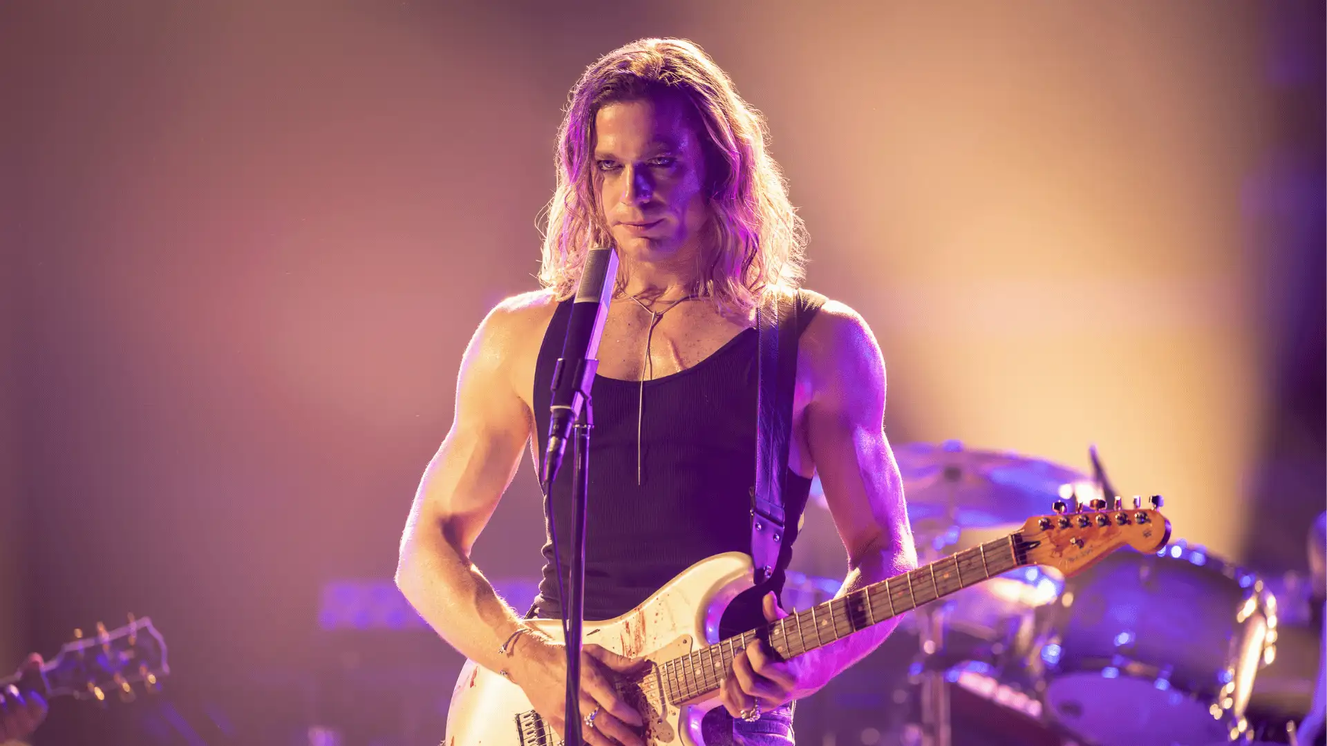 The Vampire Lestat Konzertszene: Rock-Sänger performt mit umgehangener Gitarre vor Hintergrundbeleuchteter Konzertbühne.