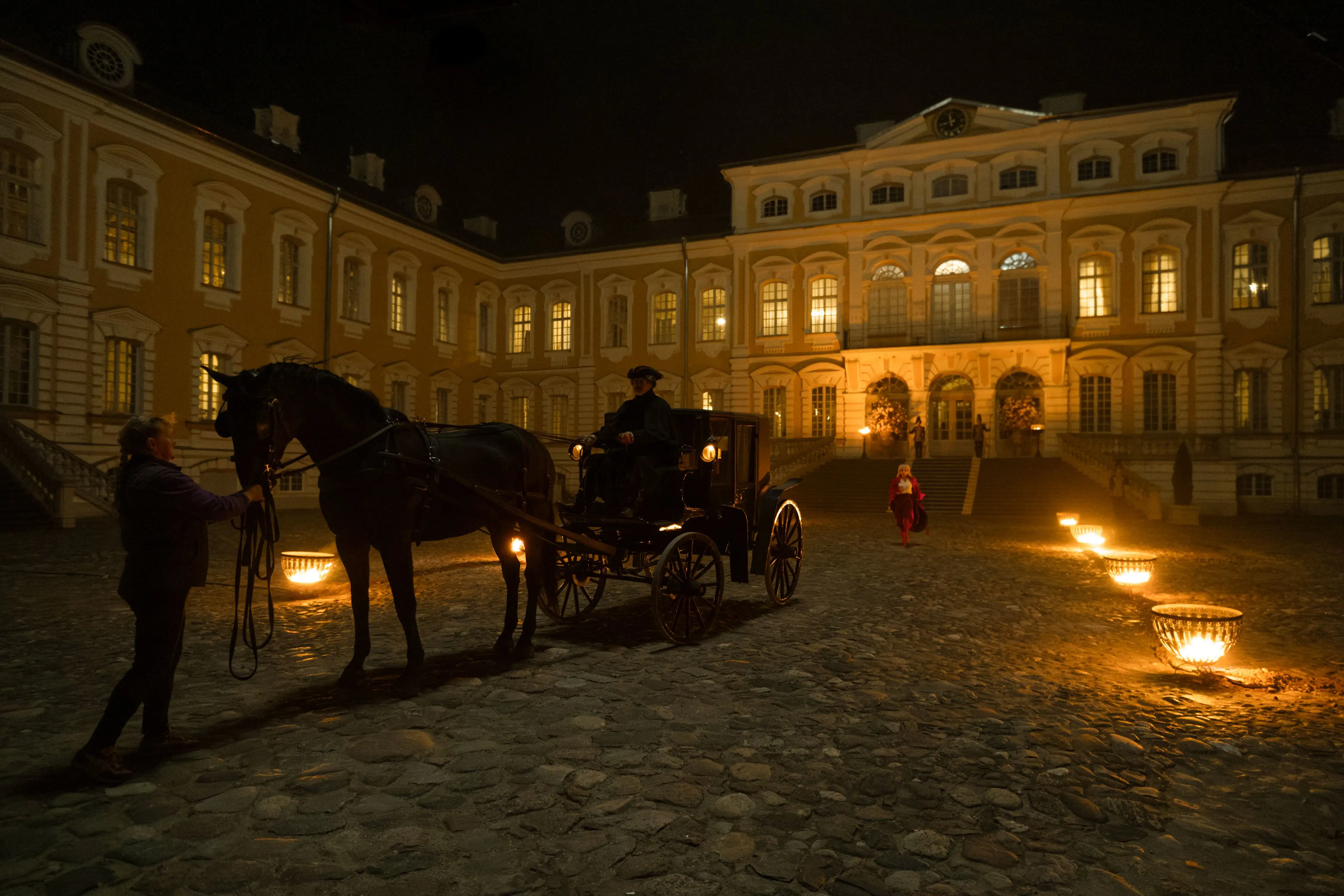 Behind the Scenes Mozart/Mozart. Eine Pferdekutsche nachts vor einem mit Kerzen belichtetes Schloss.