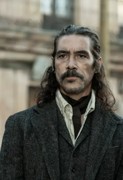 Óscar Jaenada als Federico The Walking Dead. Darly Dixon.Er trägt ein lila ein dunkles Sakko mit einem gillet in gleicher Farbe. Darunter trägt er ein beiges Hemd, um seinen Hals hat er ein Halstuch.