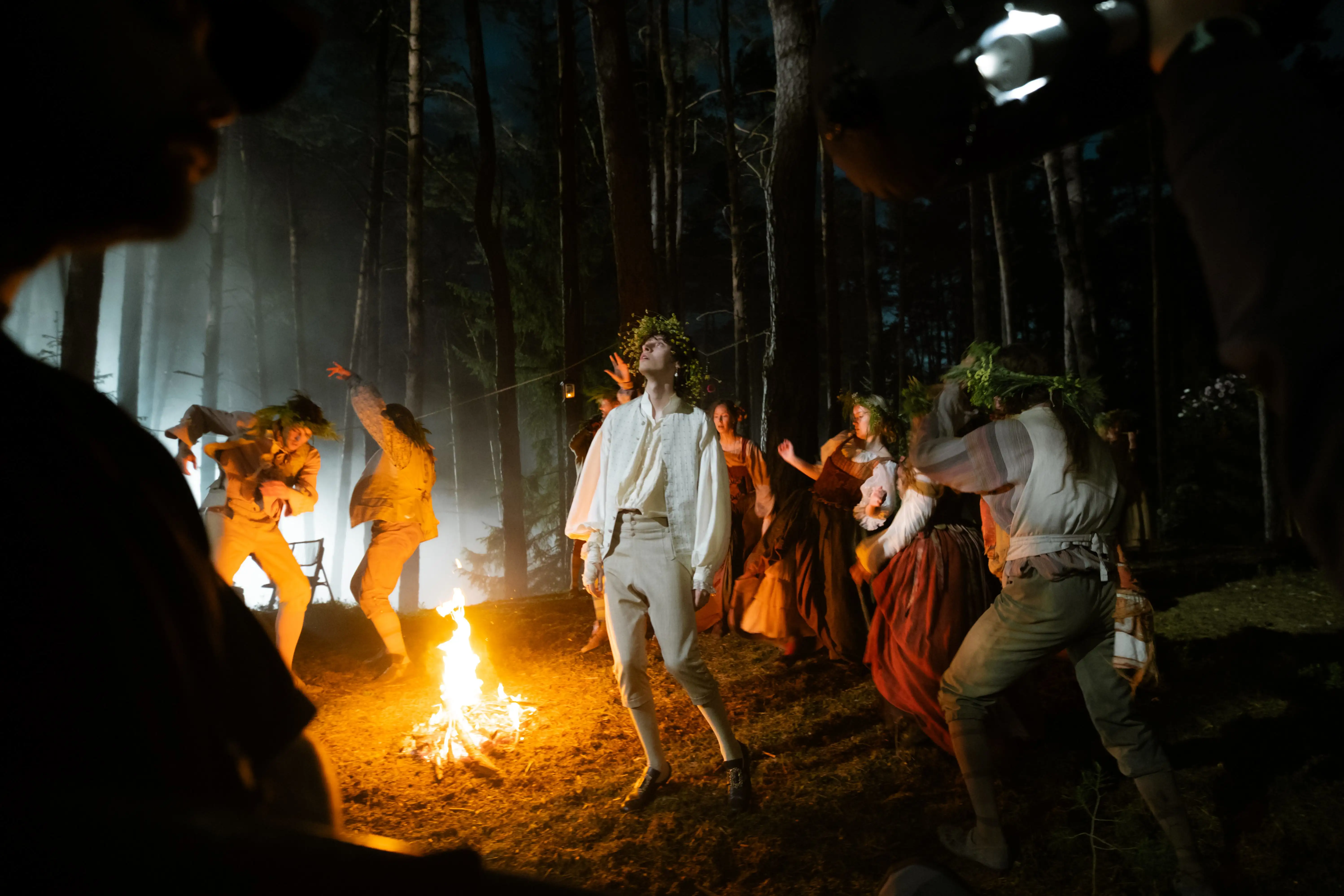 Behind the Scenes Foto Mozart/Mozart. Es ist ein Lagerfeuer im Wald zu sehen, Figuren im Stil des 18. Hahrhunderts sind abgebildet.