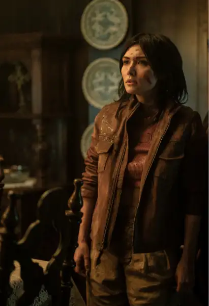 Daniella Pineda als Idalia in Tales of the Waling Dead. Sie trägt eine braune Jacke und ein braunes Hemd darunter. Sie ist bllutbefleckt und hat einen besorgten Blick.