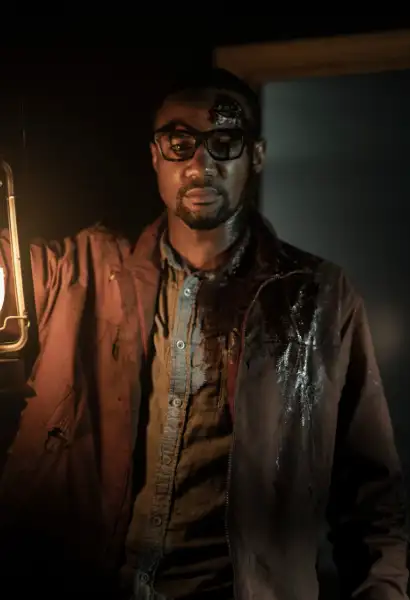 Jessie T. Usher als Davon in Tales of the Waling Dead. Er trägt eine Brille. Sein brauner Mantel ist blutgefleckt, sein weißes Hemd hat auch Blutflecken. In Seiner Hand hält er eine Laterne.