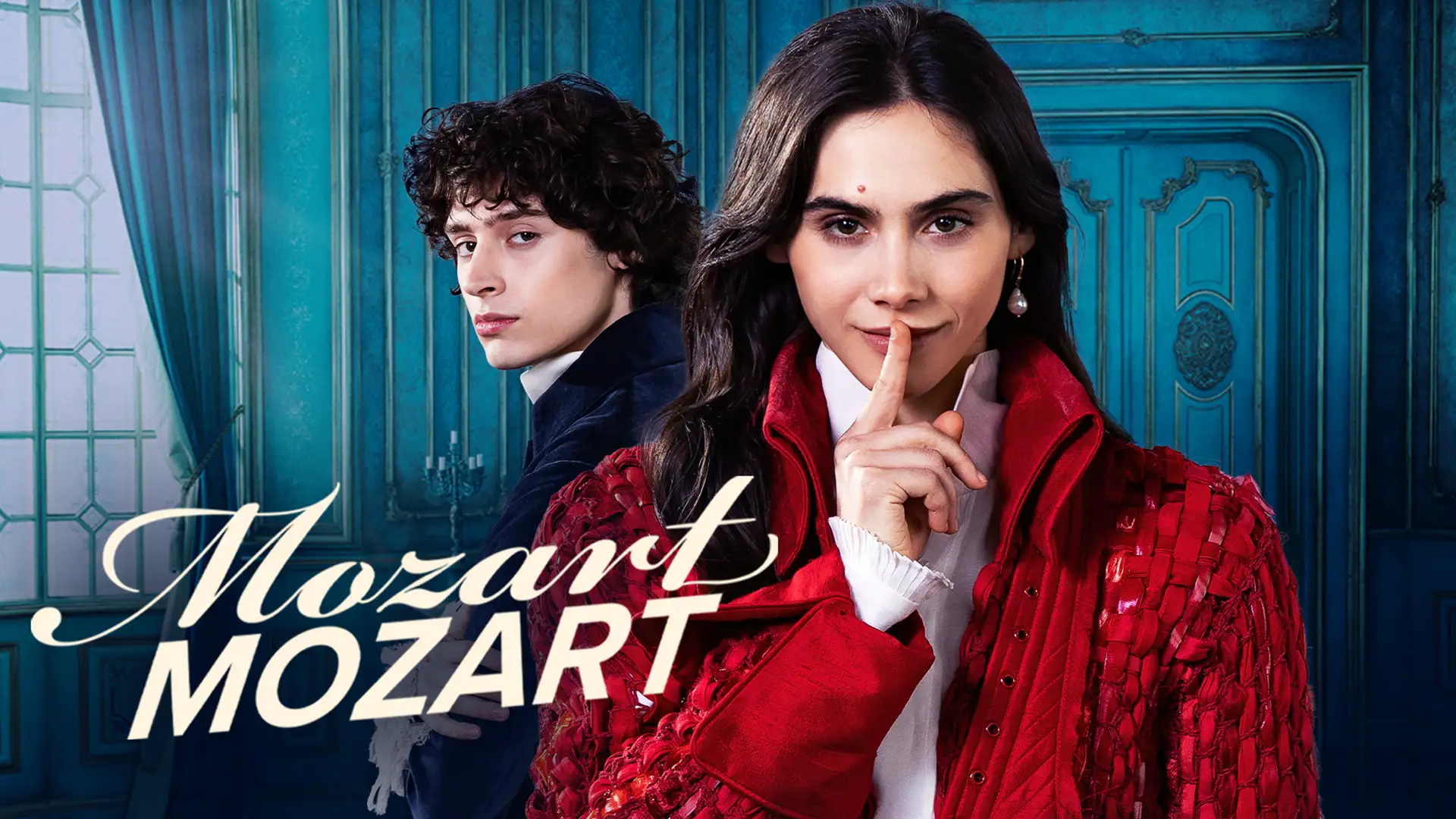 Havana Joy Braun und Eren M. Güvenci als Anna Maria und Wolfgang Mozart. Im Bild ist der Text Mozart Mozart zu sehen. Havana trägt einen roten Mantel aus dem 18. Jahrhundert, Eren einen blauen Mantel. Havana hält ihren Finger vor dem Mund, siganlisiert schweigen.