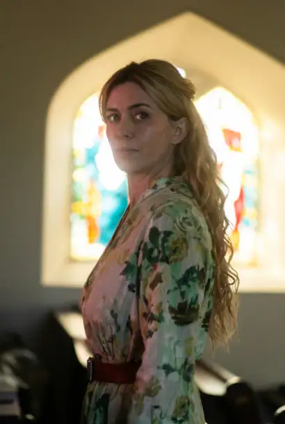 Eve Miles  in einem bunten Kleid as Rebecca in Coldwater. Sie ist in einer Kirche und steht vor einem bunten Glas..
