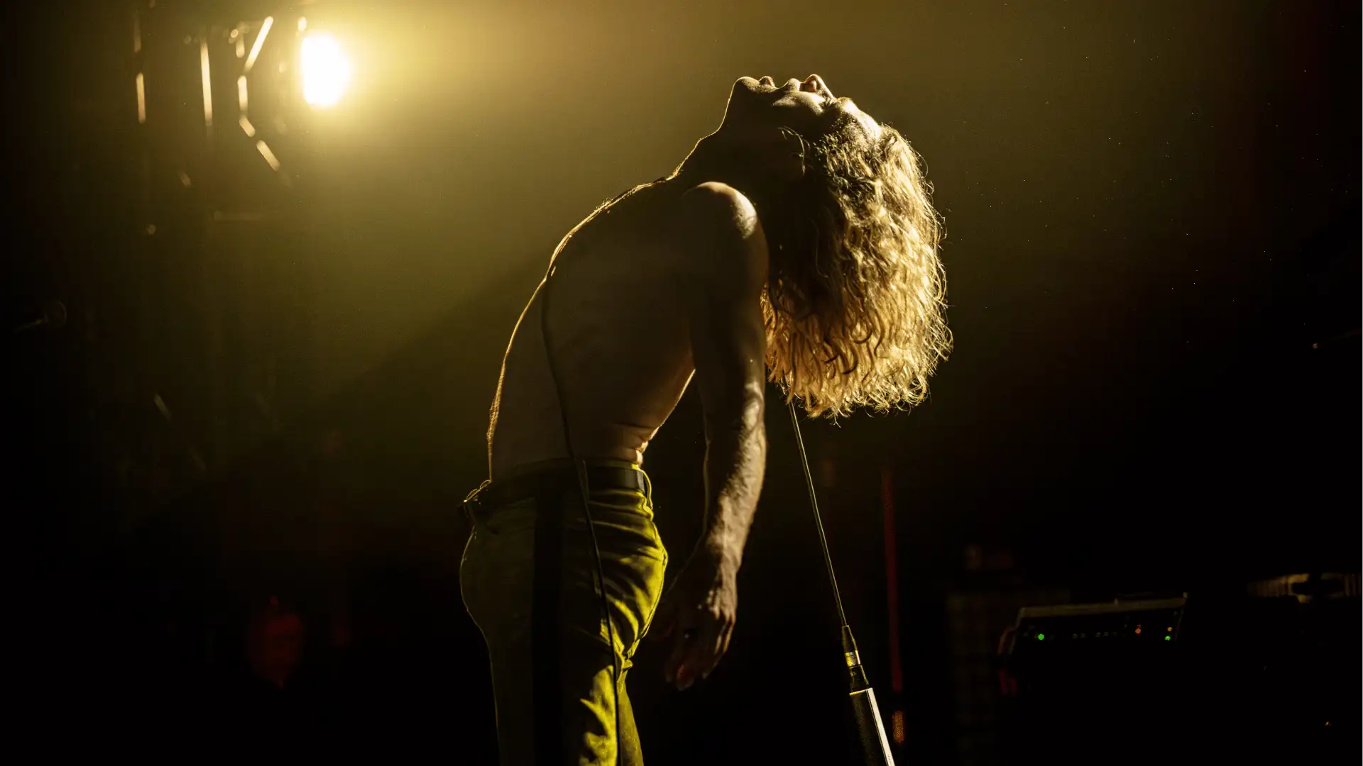 The Vampire Lestat Konzertszene: Rock-Sänger wirft seinen Oberkörper zurück während er auf abgedunkelter Bühne performt.