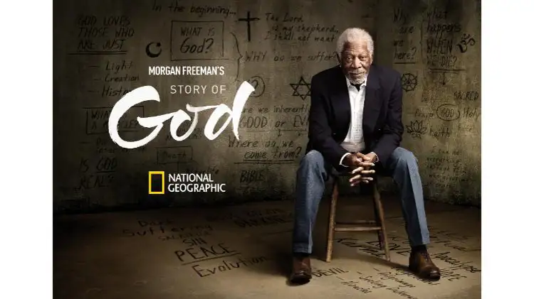 Plakat „Story of God“ mit Morgan Freeman, er trägt blaue Jeans, ein weißes Hemd und ein scwarzes Sakko. Links sieht man den Titel, darunter ist das National Geographic Logo. Im Hintergrund sind Wände auf denen Fragen
