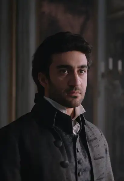 Eidin Jalali als Antonio Salieri in Mozart/Mozart. Er trägt ein dunkles Gillet und einen dunkel Mantel darüber. Im Hintergrund ist eine Wand und ein Kerzenständer zu sehen.