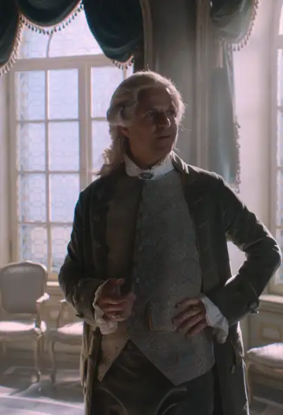Phillip Hochmaier als Kaiser Joseph der Zweite in Mozart/Mozart. Er trägt eine Perücke, ein graues Gillet und einen Braunen Mantel. Sein Blick zeigt Interesse.