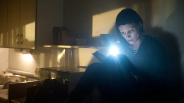 Foto aus Verblendung. Rooney Mara als Lisbeth sitzt im Dunkel und liest mit einer Taschenlampe ein Dokument.