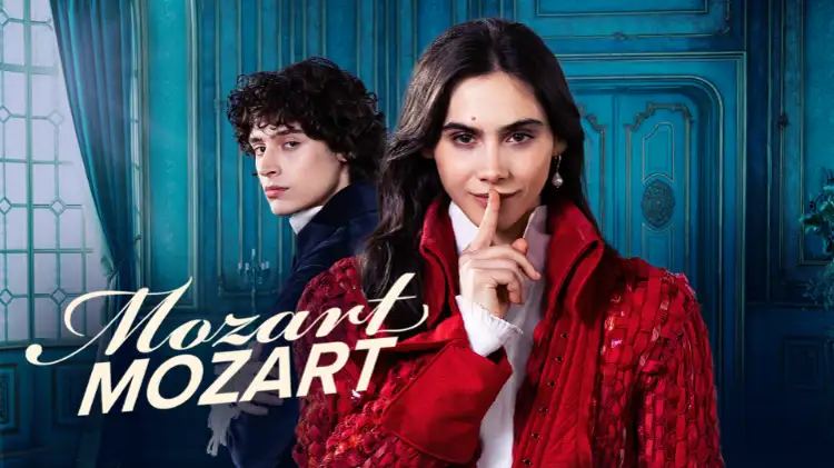 Havana Joy Braun und Eren M. Güvenci als Anna Maria und Wolfgang Mozart. Im Bild ist der Text Mozart Mozart zu sehen. Havana trägt einen roten Mantel aus dem 18. Jahrhundert, Eren einen blauen Mantel. Havana hält ihren Finger vor dem Mund, siganlisiert schweigen.